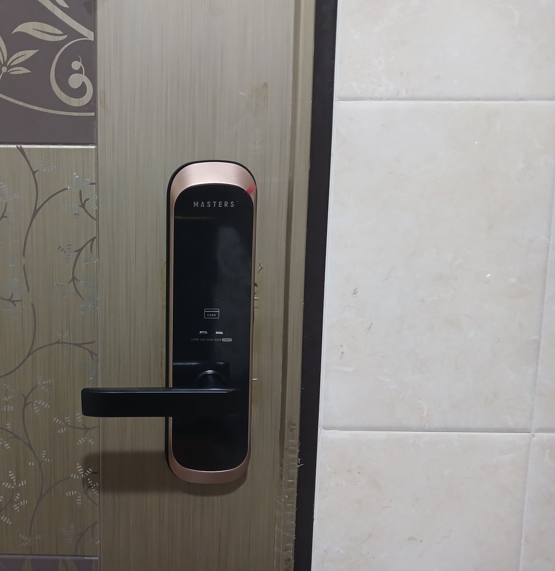 상록구 사동 출장 — 꽃무늬 문에 단 구리빛 테 검은 레버형 도어락과 오른쪽 크림색 타일 벽