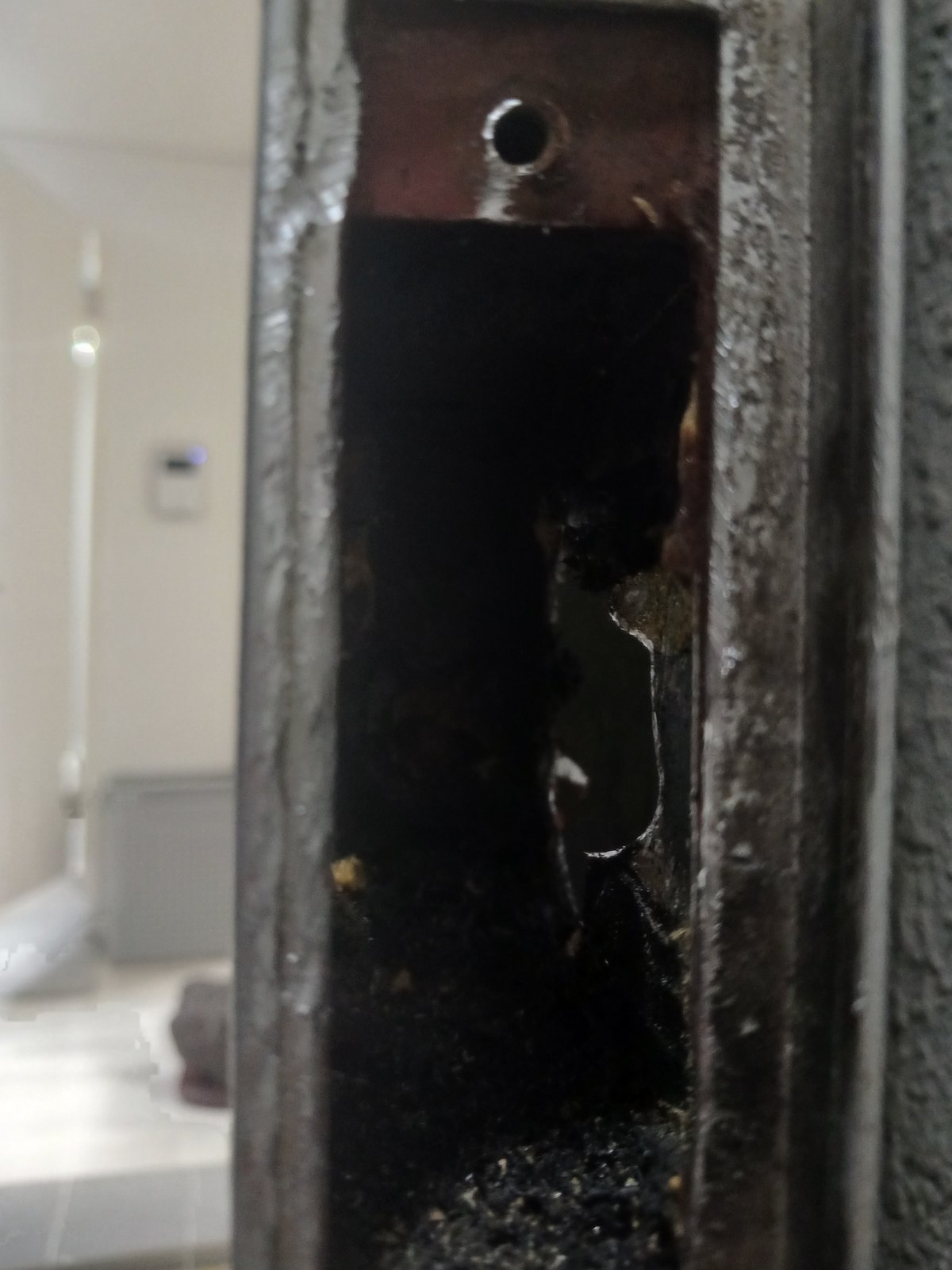 상록구 사이동 출장 — 문 옆면에 뚫린 네모난 구멍 속, 위쪽 나사 구멍과 바닥에 쌓인 검은 가루